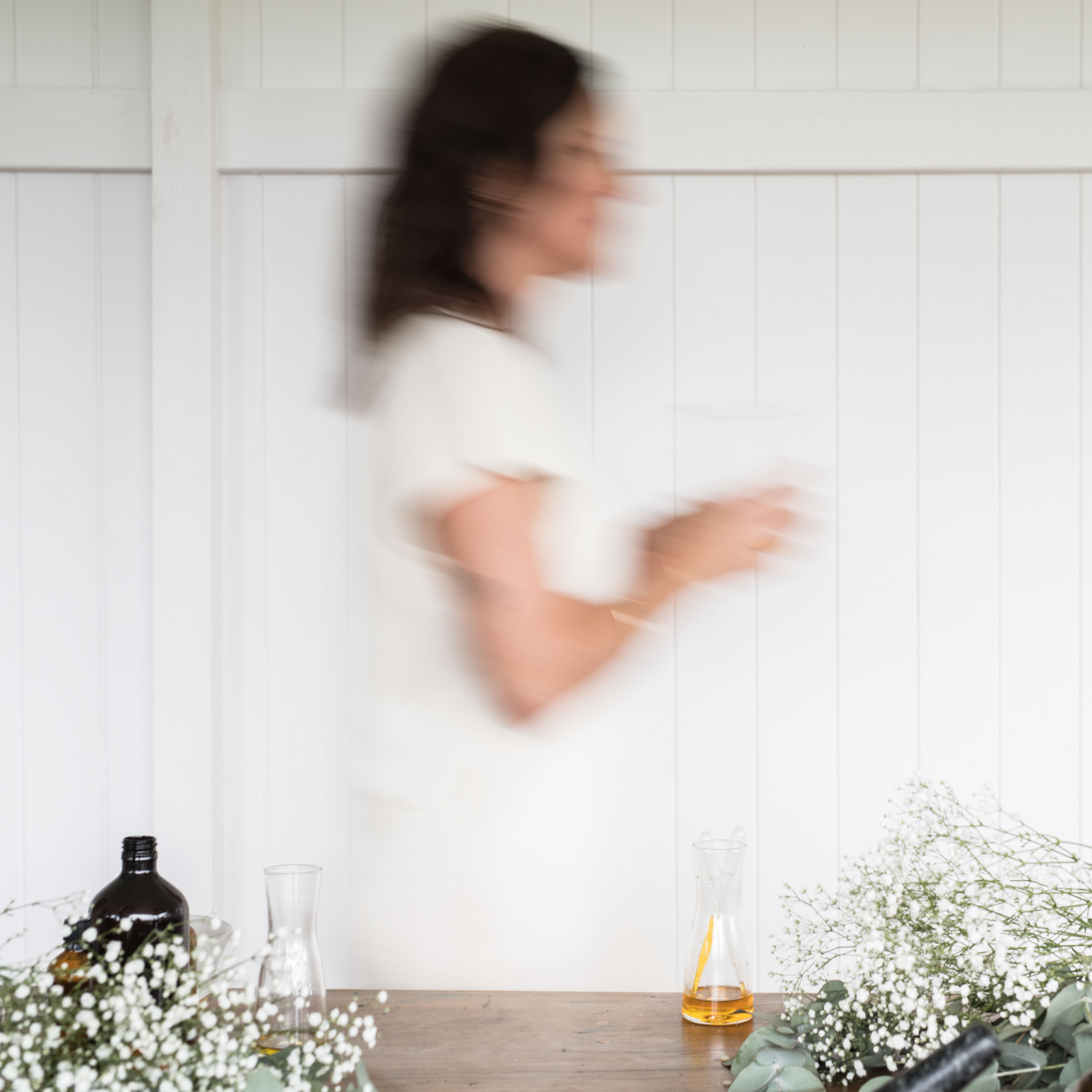 Decorative image of female walking by a table of flowers and oil