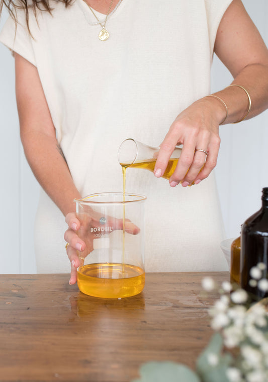 Female preparing product ingredients with a jar and beaker of oil